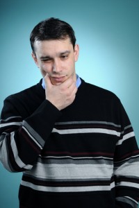 young man in large sweater holds his jaw due to pain