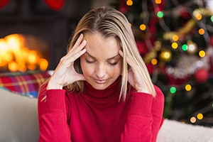 Photo of a young blonde woman sitting in front of a Christmas background, suffering from a headache.