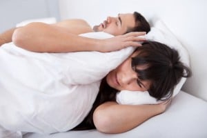 Woman covering her ears with a pillow to avoid hearing her husband's snoring.