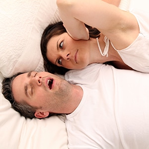 annoyed woman covering her ears with snoring husband next to her