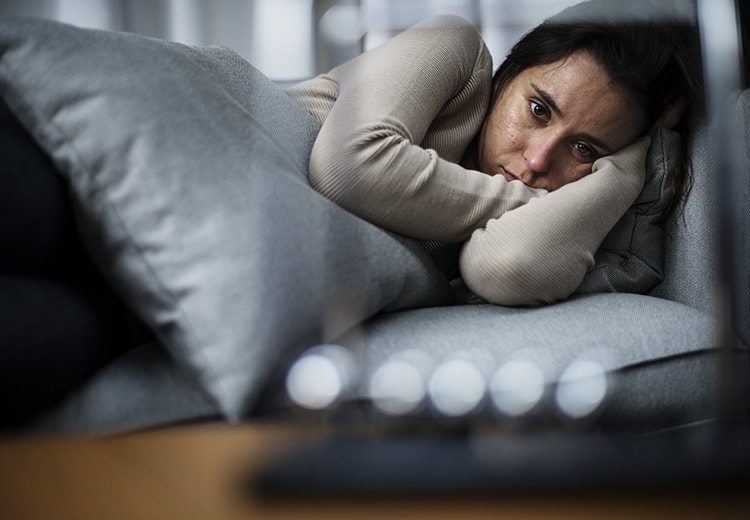 A woman suffering from depression stares blankly while lying in bed. Could Treating Sleep Apnea Help with Depression?
