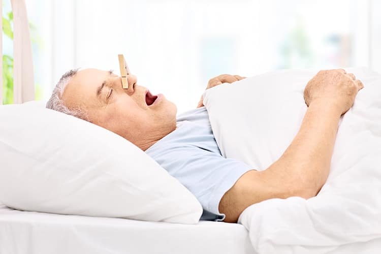 Senior sleeping with a clothespin on his nose, preventing him from snoring through his nose. There are other alternatives to this when you schedule a consultation with Denver Sleep Dentist Dr. Kevin Berry. 