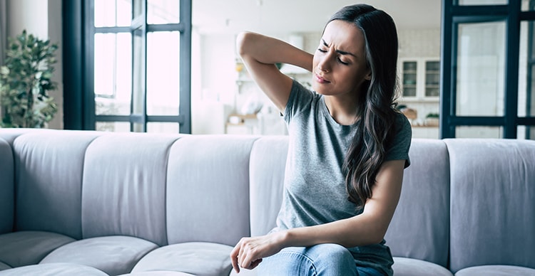 Severe woman pain in head and neck while sitting on the couch at home. TMJ flare-ups can be disabling. So what do you have to do between TMJ attacks?