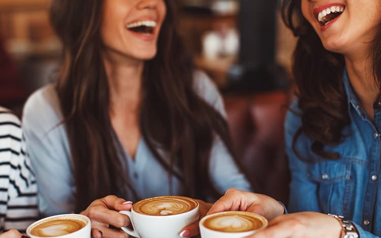 Three young women enjoy coffee at a coffee shop. Sure, it tastes great and allows you time to talk, but is it causing you migraines?