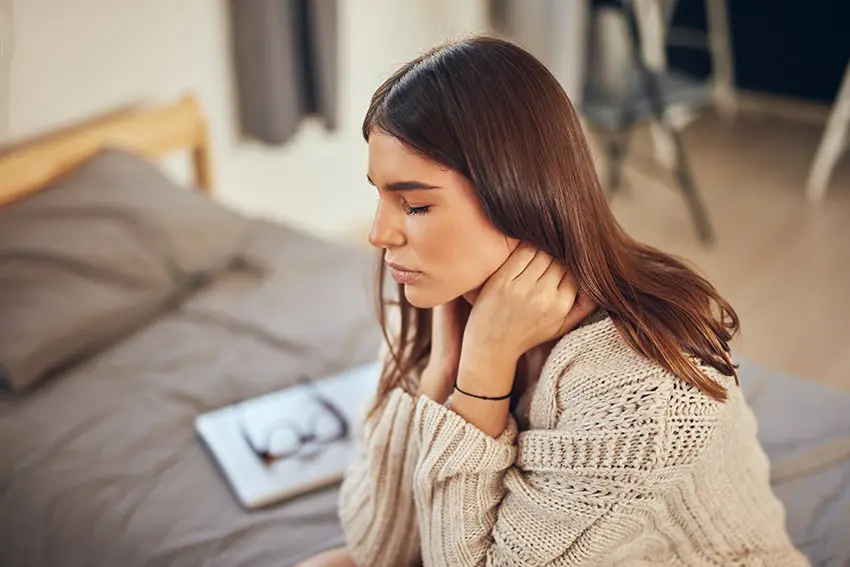 young lady sits on the couch rubbing her neck due to pain