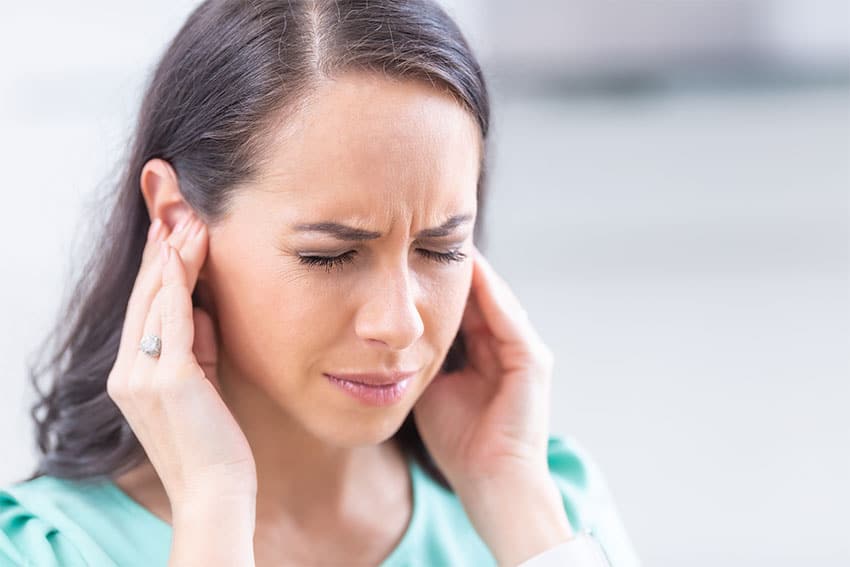 woman holding her ears due to ringing (tinnitus)